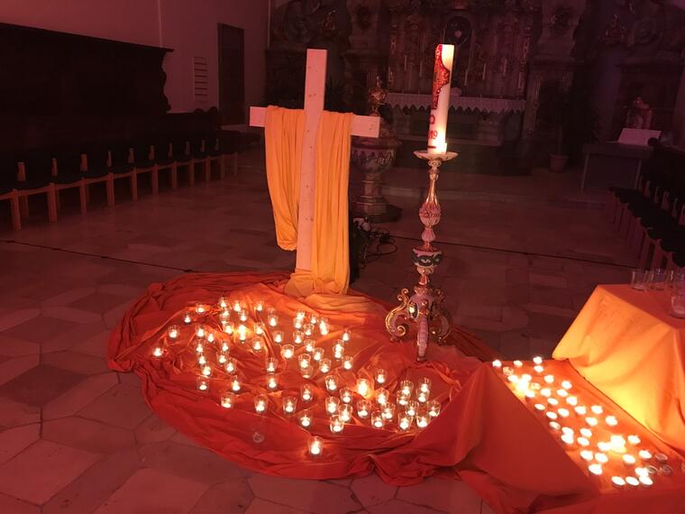 Brennende Teelichter vor einem Kreuz